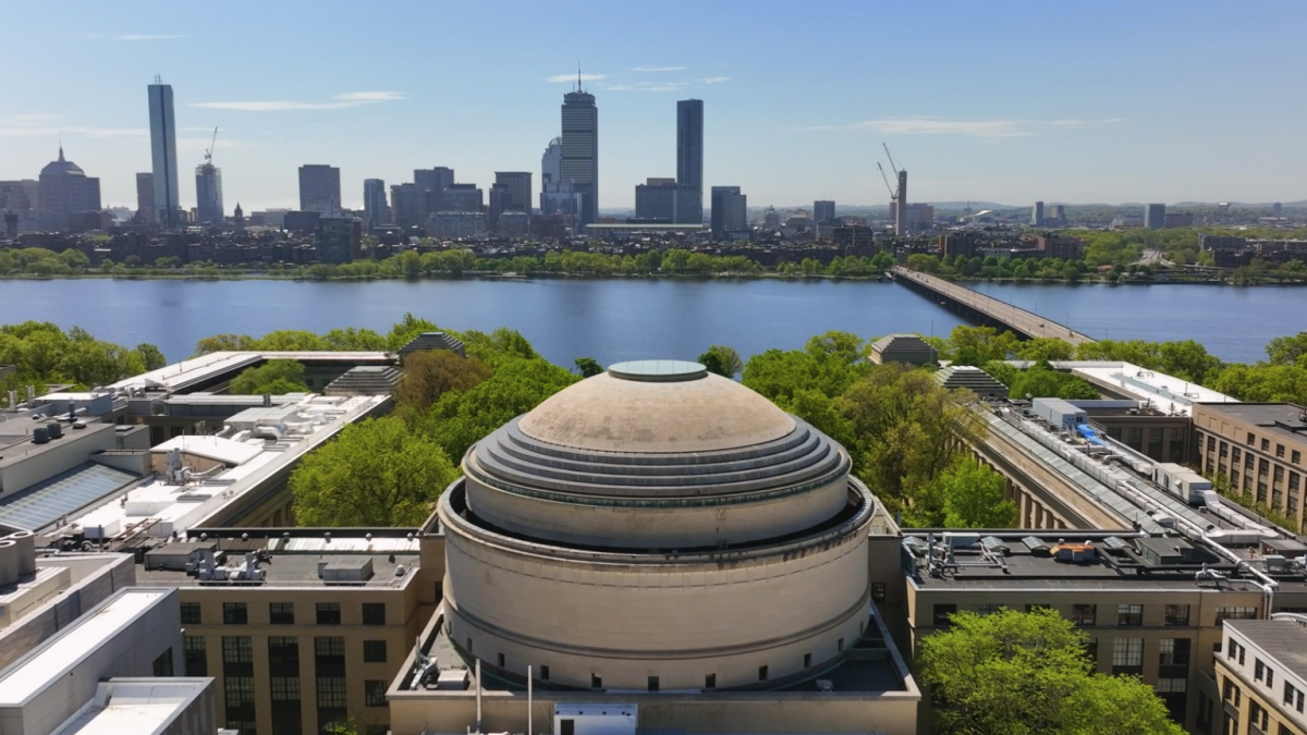 A large, domed building with a cityscape in the background. The dome has a circular base and a tall, rounded top. The cityscape includes tall skyscrapers and a river.