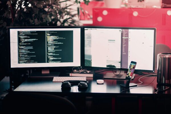 Modern dual-monitor workstation setup featuring coding on one screen, productivity tools on the other, and accessories like headphones and a smartphone for seamless multitasking.