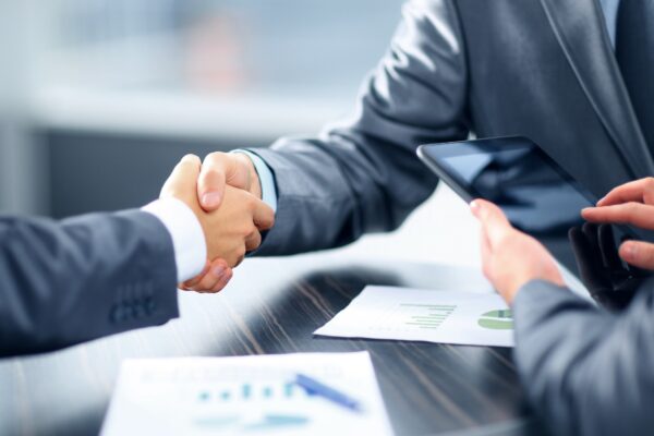 Two business professionals shaking hands over a conference table, symbolizing agreement and collaboration in a professional setting.