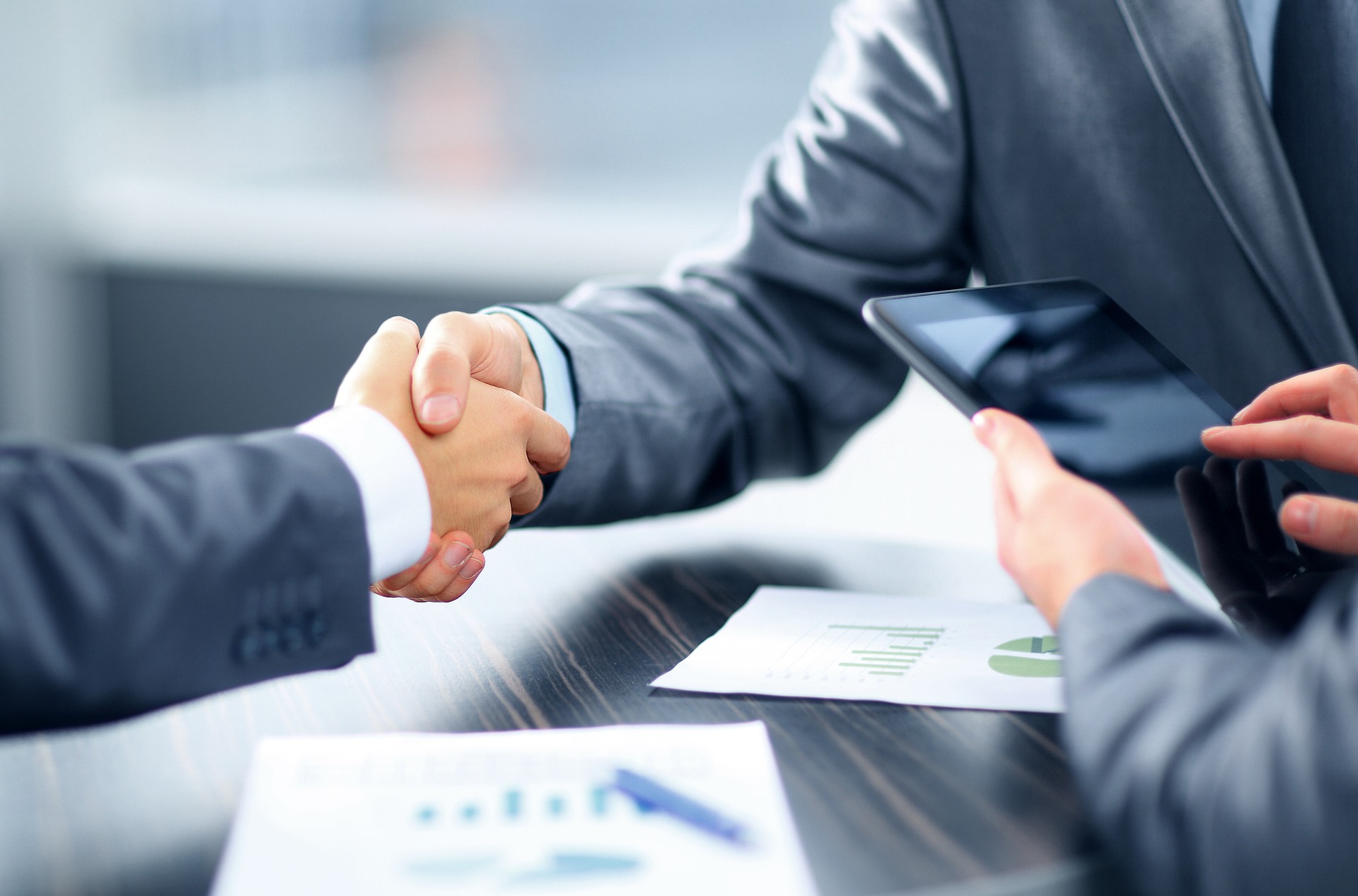 Two business professionals shaking hands over a conference table, symbolizing agreement and collaboration in a professional setting.