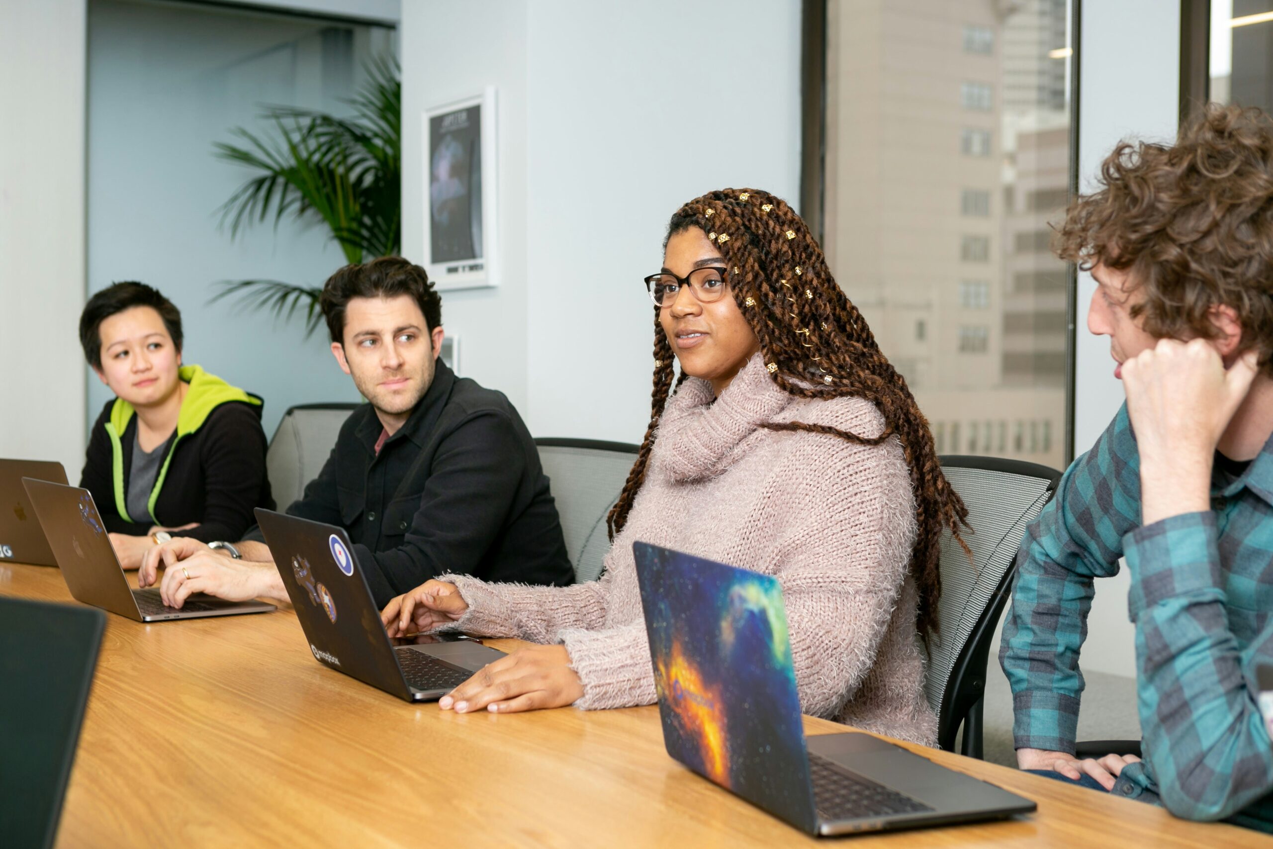 4 people with laptops on a table discussing a certain topic.