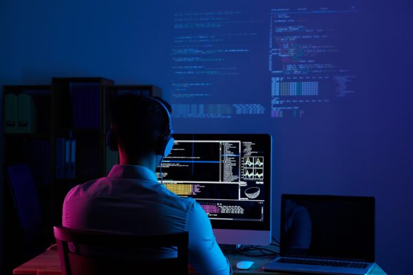 A man focused on a computer screen, seated in a dimly lit room, creating an atmosphere of concentration and solitude.