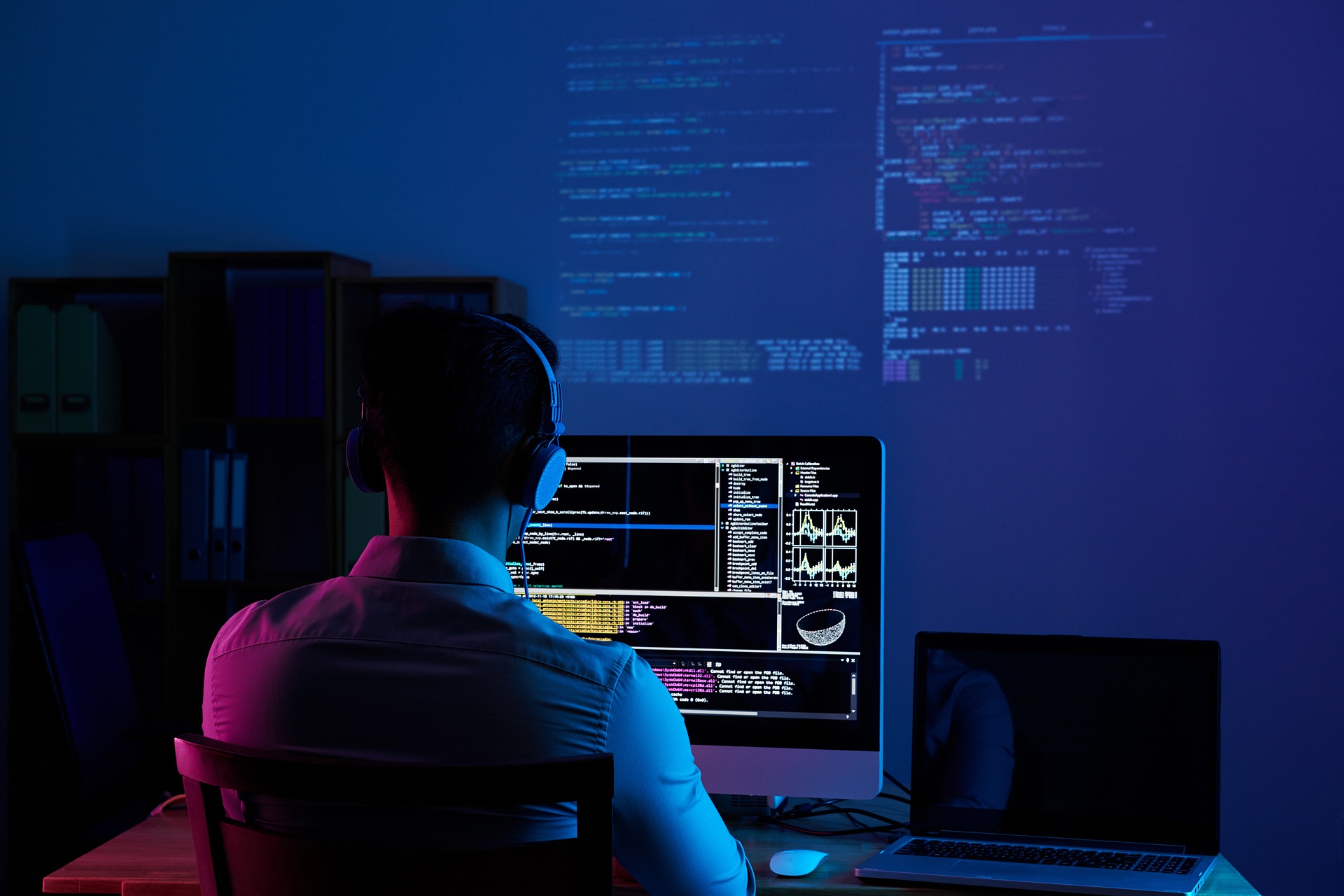 A man focused on a computer screen, seated in a dimly lit room, creating an atmosphere of concentration and solitude.