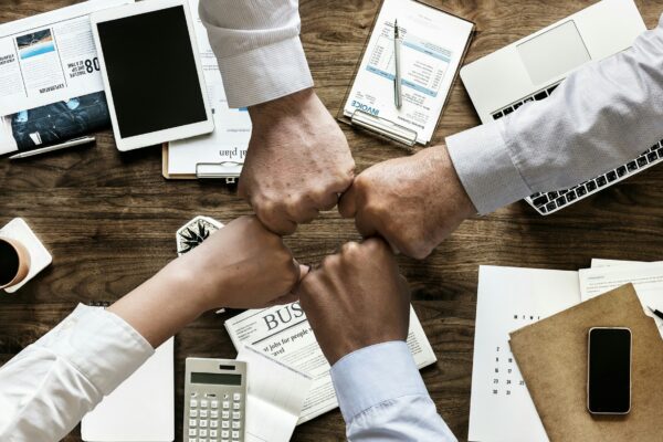 Business professionals collaborating around a table, holding hands, with papers and calculators in front of them.