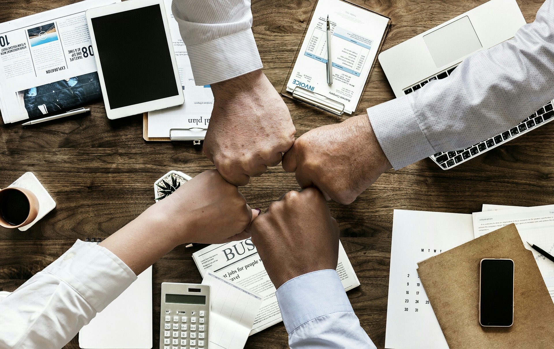 Business professionals collaborating around a table, holding hands, with papers and calculators in front of them.