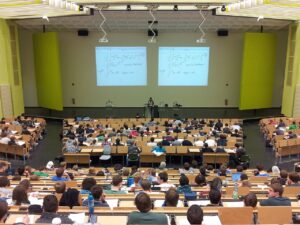 University lecture hall with students attending a math class, large screens displaying equations.