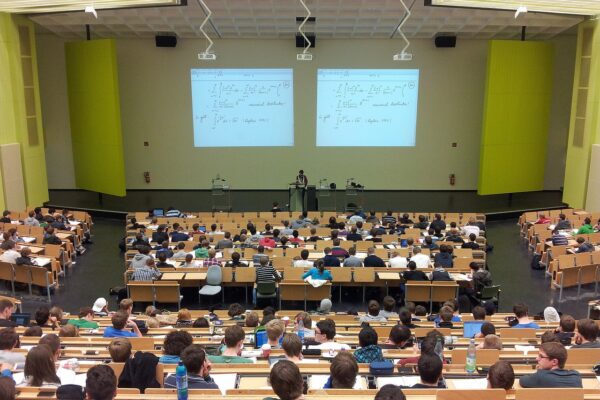 University lecture hall with students attending a math class, large screens displaying equations.