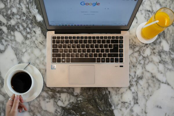 Laptop on a marble table with Google homepage, coffee, and orange juice nearby.