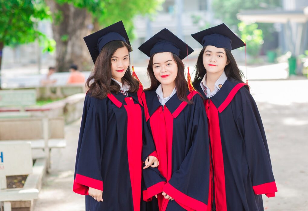 Three women in graduation gowns smiling and posing together for a celebratory photograph.