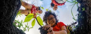 Two children are crouched down, each grasping a young plant, actively participating in planting activities outdoors.